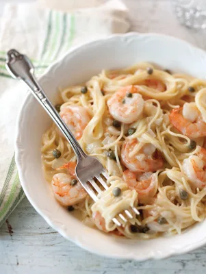 Paula Deen lemony shrimp and caper pasta, angel hair with pink shrimp and capers in a creamy lemon sauce in a white bowl with a fork