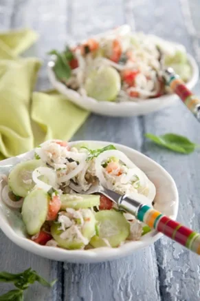 Paula Deen lighter crab salad with lump crab, cucumber slices, grape tomatoes and thin onion rings in white bowls on a blue wooden table