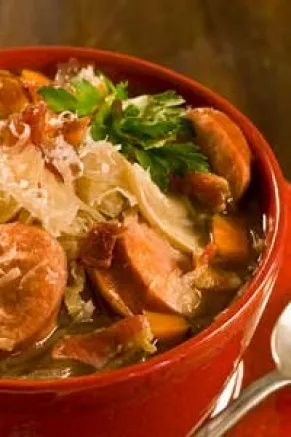 Paula Deen lighter slow cooker smoked pork, lentil and sauerkraut soup in a red bowl with sausage slices, carrots and parsley