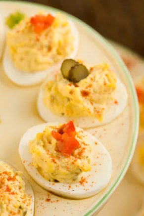 Paula Deen lighter Southern deviled eggs topped with chopped pimentos, a pickle slice and paprika on a green-rimmed plate