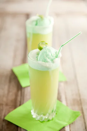 Paula Deen lime sherbet punch in tall glasses topped with a scoop of green sherbet, a lime slice and a straw