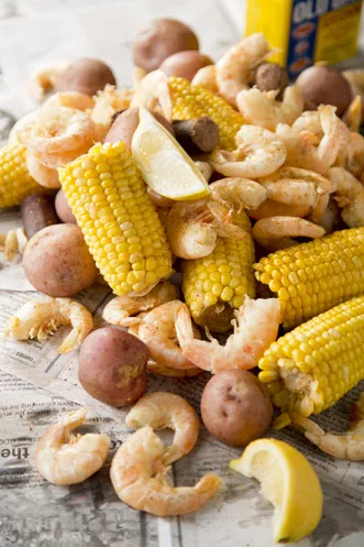 Paula Deen low country boil with shrimp, corn on the cob, red potatoes, smoked sausage and lemon wedges on newspaper