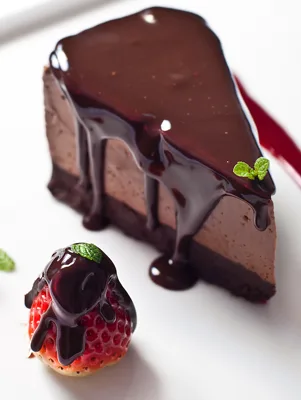 Slice of Paula Deen luscious chocolate cheesecake with glossy chocolate glaze and a chocolate-drizzled strawberry