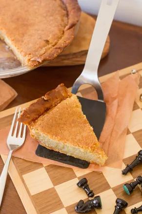 Slice of Paula Deen Mama's Chess Pie with a golden top on a pie server beside a chess board