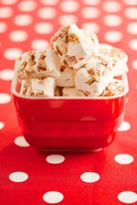 Paula Deen Mama's divinity candy, fluffy white swirls with chopped pecans, piled in a red square bowl on a red polka dot cloth