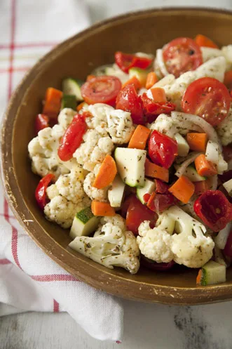 Paula Deen marinated vegetable salad with cauliflower, cherry tomatoes, zucchini and carrots in a wooden bowl