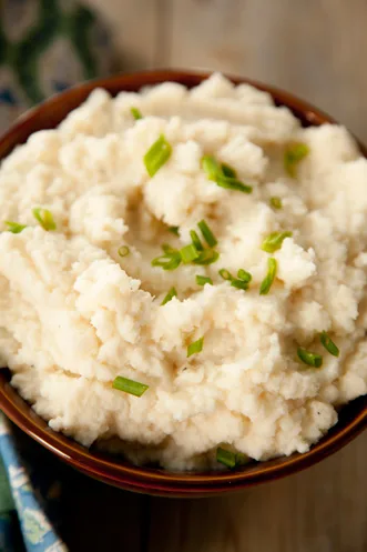 Paula Deen mashed cauliflower in a brown bowl topped with sliced fresh chives