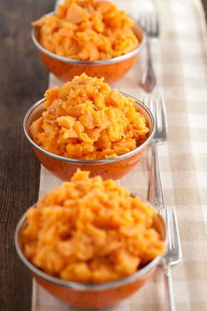 Three copper bowls of Paula Deen mashed sweet potatoes on a checkered tablecloth with forks