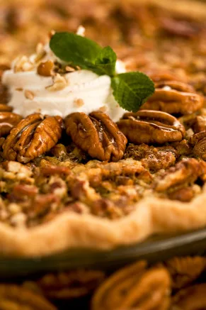 Paula Deen mystery pecan pie topped with whipped cream and a mint leaf, with toasted chopped pecans on a golden crust
