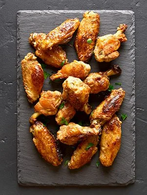 Paula Deen naked hot air fryer Southern chicken wings, golden and crispy, on a dark slate board with chopped green herbs