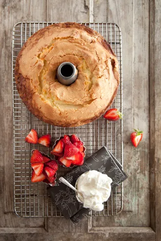 Paula Deen never-fail pound cake on a wire rack with fresh strawberries and a bowl of whipped cream