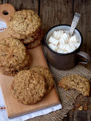 Paula Deen oatmeal raisin cookies stacked on a wooden board next to a mug of hot cocoa topped with marshmallows