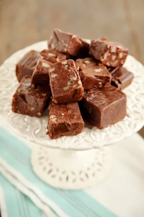 Paula Deen old time chocolate fudge squares with pecans stacked on a white cake stand