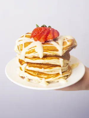 Paula Deen ooey gooey butter pancakes stacked on a white plate with a cream cheese butter drizzle and a fresh strawberry on top