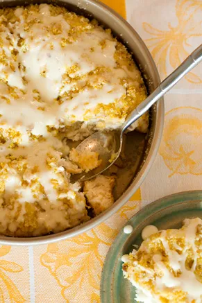 Paula Deen orange coffee cake with cream cheese glaze and walnut topping in a round pan with a serving spoon