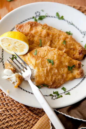 Paula Deen oven fried catfish fillets with a golden cornmeal crust, parsley and a lemon half on a white plate