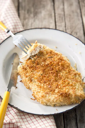 Paula Deen oven-fried chicken with a golden oatmeal crust on a white enamel plate with a yellow-handled fork and knife