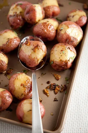 Paula Deen oven roasted red potatoes with rosemary and garlic on a baking sheet with a spoon and browned garlic bits