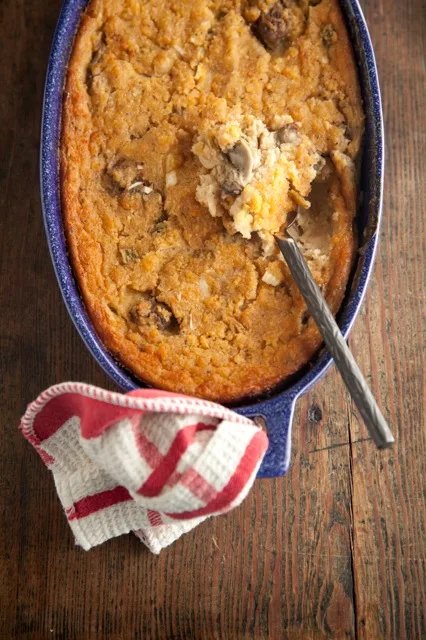 Paula Deen oyster dressing baked golden in a blue enamel dish with a spoon lifting a scoop showing oysters inside