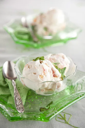 Paula Deen peach ice cream scooped into a glass dish with peach chunks and a mint sprig on a green glass plate