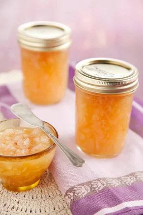 Paula Deen pear honey in sealed half-pint jars with a small bowl of golden pear honey and a spoon on a purple striped napkin