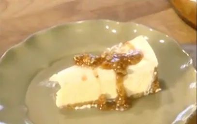 Slice of Paula Deen pecan praline cheesecake topped with glossy praline sauce on a green scalloped plate