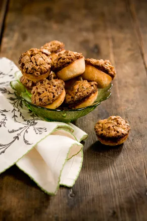 Paula Deen pecan toffee tassies piled in a green glass bowl next to a linen napkin on a rustic wooden table