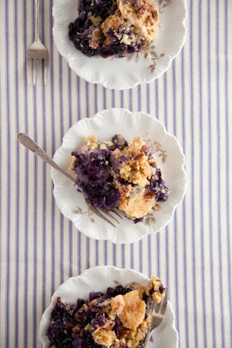 Paula Deen pineapple blueberry crunch cake served on three white floral plates with forks on a blue striped tablecloth