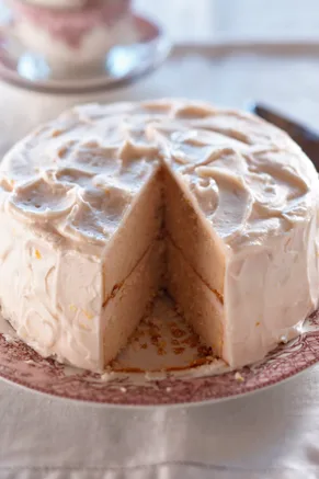 Paula Deen pink lemonade layer cake with a slice removed showing two pale pink layers and swirled pink lemonade frosting on a floral cake plate