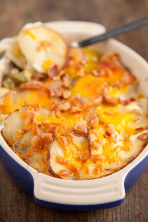 Paula Deen potato casserole with melted cheddar, sliced potatoes and crumbled bacon in a blue baking dish