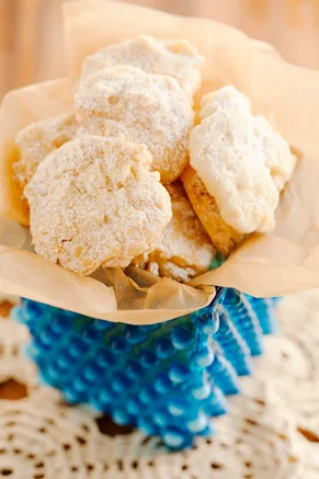 Paula Deen potato chip cookies dusted with confectioners' sugar piled in a parchment-lined blue glass dish