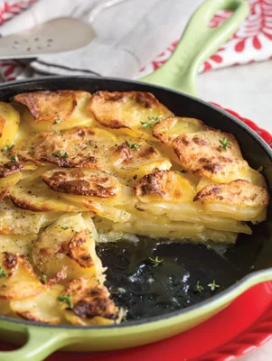 Paula Deen Potatoes Anna in a green cast iron skillet with golden crispy overlapping potato slices and fresh herbs
