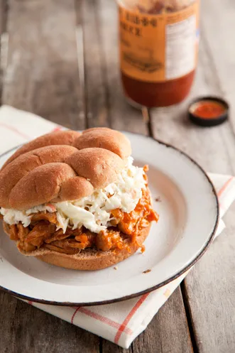 Paula Deen pulled BBQ chicken sandwich on a whole-wheat roll topped with coleslaw, served on a white enamel plate