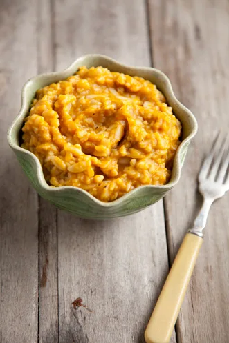 Paula Deen pumpkin orzo served in a green scalloped bowl with a fork beside it on a wooden table