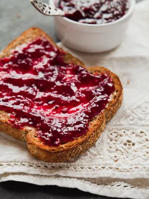 Paula Deen raspberry fig preserves spread on a slice of whole grain toast with a small bowl of jam in the background