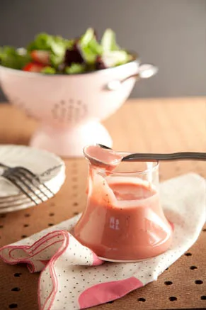 Paula Deen rhubarb salad dressing in a glass jar with a spoon, next to a pink colander of fresh salad greens