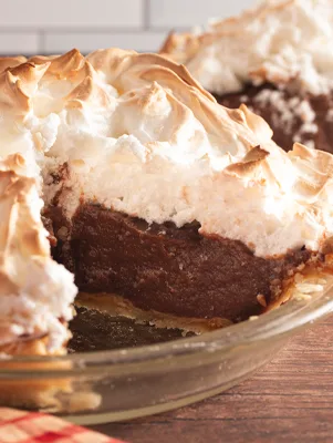 Paula Deen rich chocolate meringue pie with toasted meringue and a slice cut out of a glass pie dish