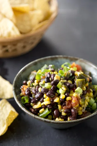 Paula Deen roasted corn, pepper, and black bean salsa in a rustic bowl with tortilla chips beside it