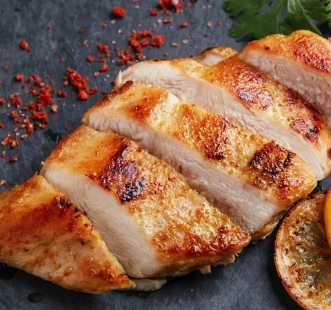 Paula Deen roasted spicy mayonnaise chicken breasts sliced and golden brown with paprika, cayenne flakes and lemon halves on a dark slate board