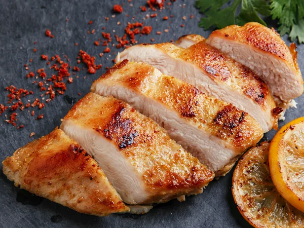 Paula Deen roasted spicy mayonnaise chicken breasts sliced and golden brown with paprika, cayenne flakes and lemon halves on a dark slate board