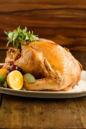 Paula Deen roasted turkey recipe with golden skin on a white platter, garnished with fresh herbs, orange halves, sage and grapes