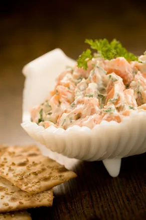 Paula Deen salmon dip served in a white shell-shaped dish with a parsley garnish and sesame crackers beside it