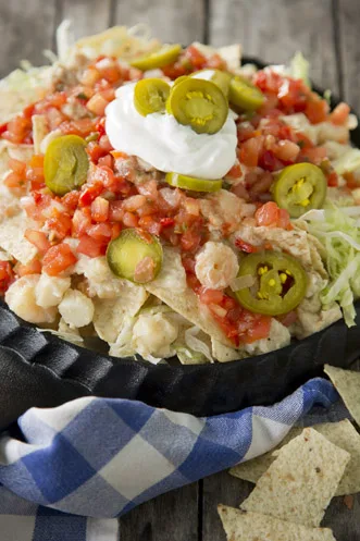 Paula Deen seafood nachos topped with shredded lettuce, pico de gallo, pickled jalapeno slices and sour cream in a black cast iron pan