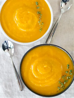 Two bowls of Paula Deen secret ingredient butternut squash soup, smooth and golden orange, garnished with fresh thyme sprigs and served with spoons