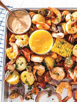Paula Deen sheet pan shrimp boil with shrimp, corn, potatoes, sausage and mushrooms on a baking sheet with butter and remoulade