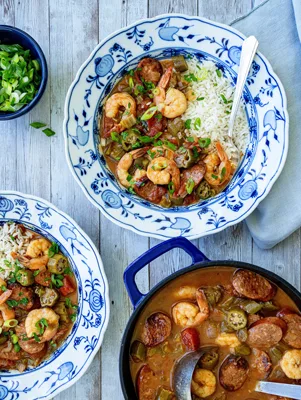 Paula Deen shrimp gumbo with andouille sausage and okra in a blue Dutch oven, served over rice in blue and white bowls