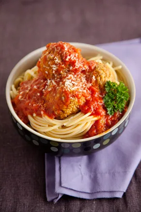 Paula Deen slow cooker cheese stuffed meatballs and sauce over spaghetti in a polka dot bowl topped with grated Parmesan and parsley