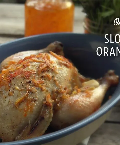 Paula Deen slow cooker orange chicken in a blue dish topped with orange zest and rosemary, with orange slices beside it