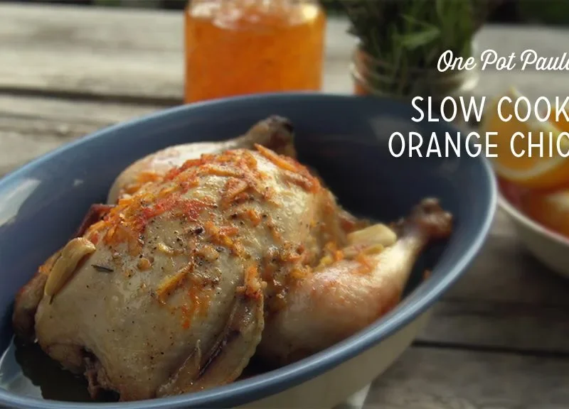 Paula Deen slow cooker orange chicken in a blue dish topped with orange zest and rosemary, with orange slices beside it