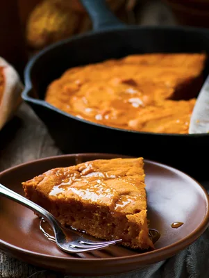 Paula Deen souffled pumpkin pancake wedge drizzled with syrup on a brown plate beside a cast iron skillet